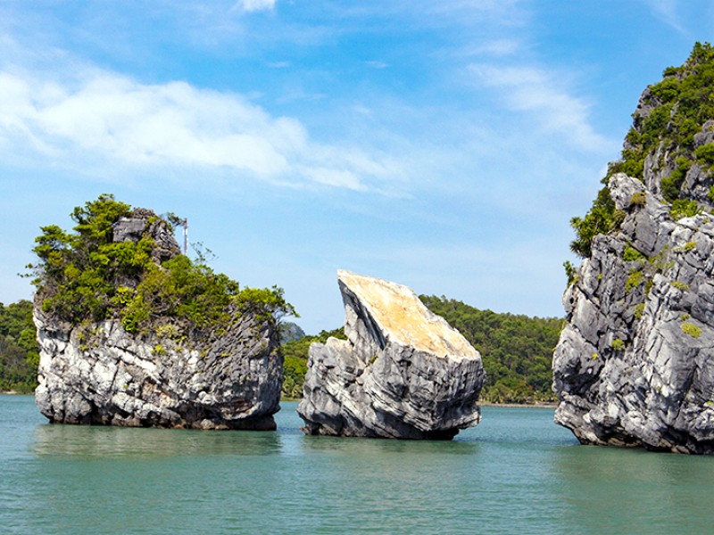 Cặp đá đôi nổi lên từ làn nước êm đềm tại vịnh Hòn Thiên Nga, với cây xanh mọc trên bề mặt đá.