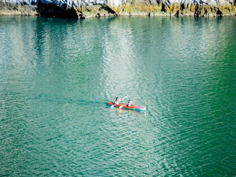 Hai người đang chèo thuyền kayak qua làn nước yên bình của hồ Ba Hầm tại Vịnh Lan Hạ, bao quanh bởi các vách đá vôi.