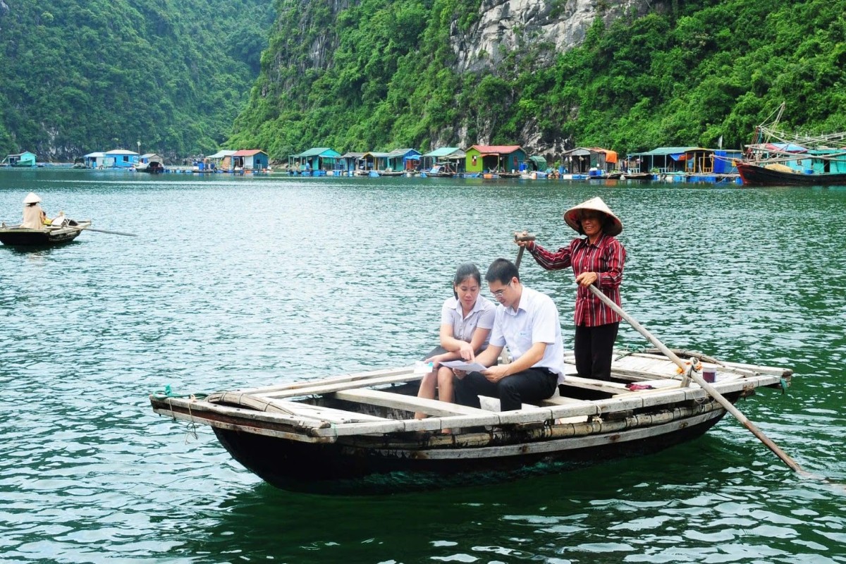 Một chiếc thuyền tre lướt qua Làng Chài Cửa Vạn, với các vách đá vôi hùng vĩ ở phía xa.