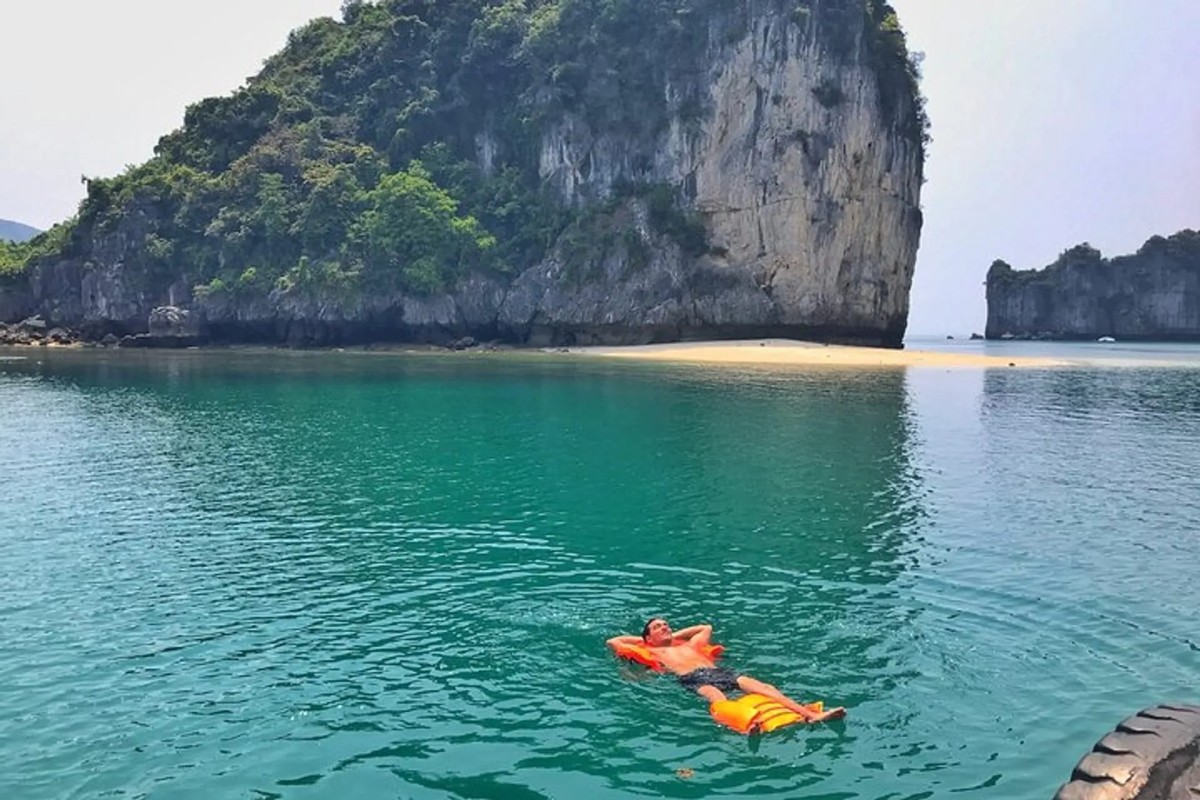 Một du khách nổi trên làn nước yên bình tại Trà Báu ở Vịnh Lan Hạ, được bao quanh bởi các vách đá vôi.